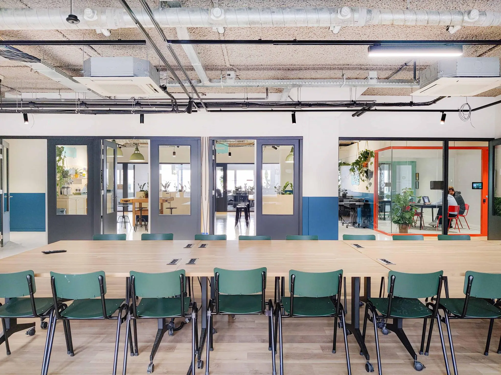 Vergaderruimte aan de Aert van Nesstraat met opklapbare stoelen, houten tafel en zicht op meerdere werkruimtes en kantoren.